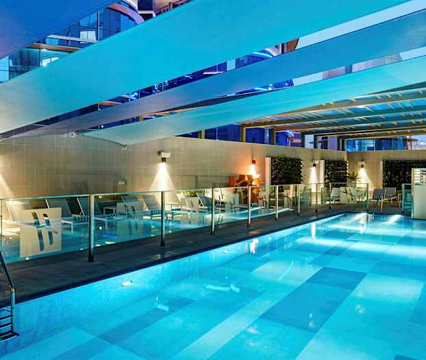 Sisäuima-allas valaistuksella. Altaan ympärillä on lepotuoleja ja lasikaiteita. (Tekoälyn luoma teksti)