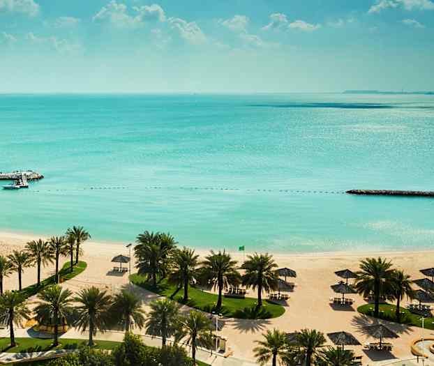 Hiekkaranta, jossa valkoisia aurinkovarjoja, palmupuita ja turkoosi vesi. (Tekoälyn luoma teksti)