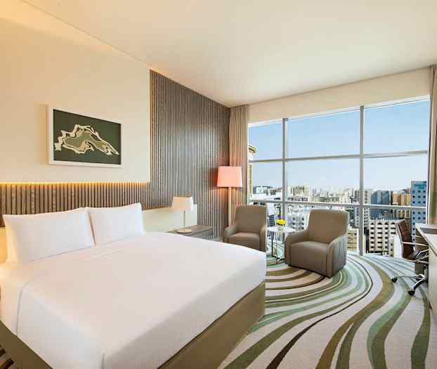 Moderni hotellihuone, jossa on iso sänky ja kaksi tuolia ikkunan edessä. (Tekoälyn luoma teksti)