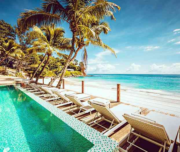 Ulkouima-allas aurinkotuoleilla hiekkarannan äärellä kirkkaan sinisen veden äärellä. (Tekoälyn luoma teksti)