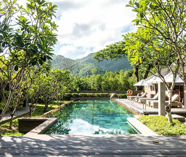 Kuva uima-altaasta, jota ympäröivät vehreys ja aurinkotuolit, taustalla näkyy kukkuloita ja puita. (Tekoälyn luoma teksti)