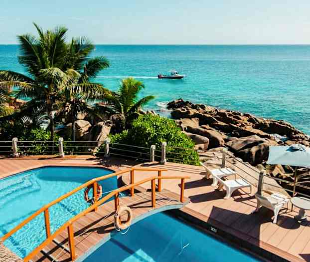 Uima-allasalue, josta on näkymä merelle, ympärillä palmuja ja kalliota. (Tekoälyn luoma teksti)