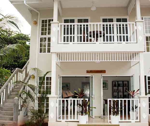 Kaksikerroksisen rakennuksen sisäänkäynti, jossa on kyltti sisäänkäynnin kohdalla, jossa lukee "Vastaanotto", sekä ympäröivä puutarha. (Tekoälyn luoma teksti)