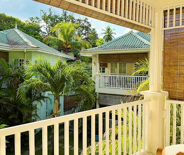 Näköala parvekkeelta, josta näkyy vehreä alue pastellinvärisine taloineen ja palmupuineen. (Tekoälyn luoma teksti)