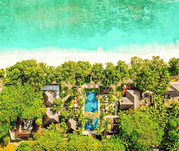 Ilmakuva hotellista rannalla, jossa on uima-allas ja jota ympäröi vehreä luonto. (Tekoälyn luoma teksti)