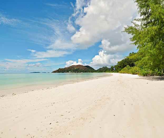 Hiekkaranta, jossa kirkasta vettä ja vihreää kasvillisuutta taustalla. Horisontissa näkyy vuorenhuippu. (Tekoälyn luoma teksti)