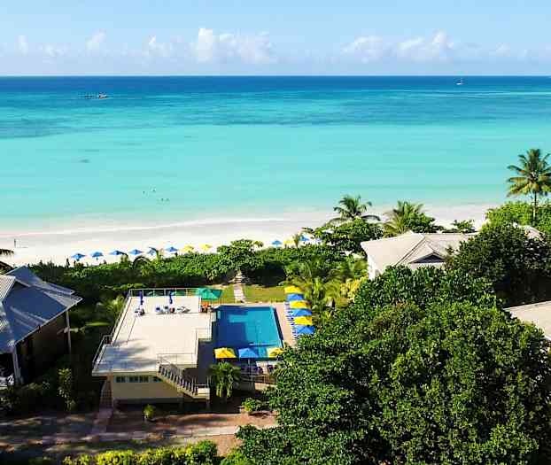 Lomahotelli rannalla, turkoosia vettä ja vehreää ympäristöä. (Tekoälyn luoma teksti)