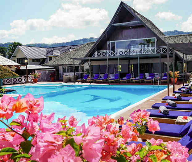 Uima-allasalue aurinkotuoleilla ja kukilla, rakennuksia taustalla. (Tekoälyn luoma teksti)