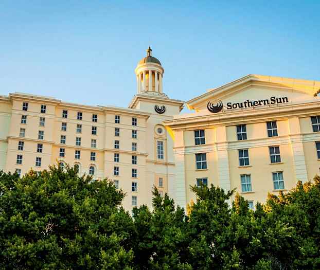 Vaalea monikerroksinen rakennus ja torni näkyvät vehreiden puiden takaa. (Tekoälyn luoma teksti)