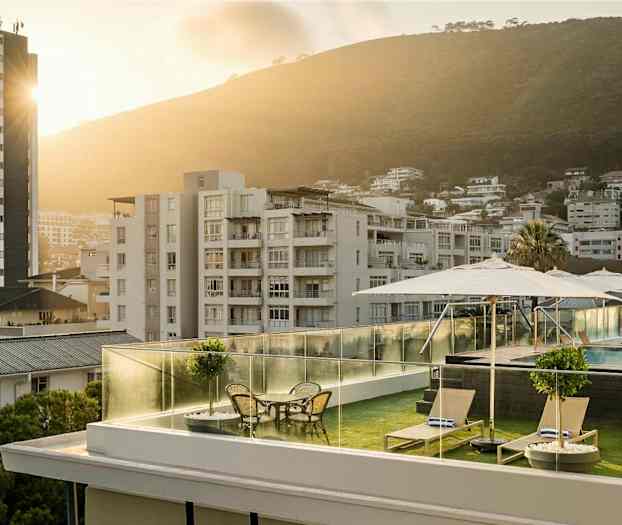 Kattoterassi aurinkotuoleineen, pöytineen ja varjoineen, taustalla uima-allas ja vehreitä kukkuloita sisältävää kaupunkimaisemaa. (Tekoälyn luoma teksti)