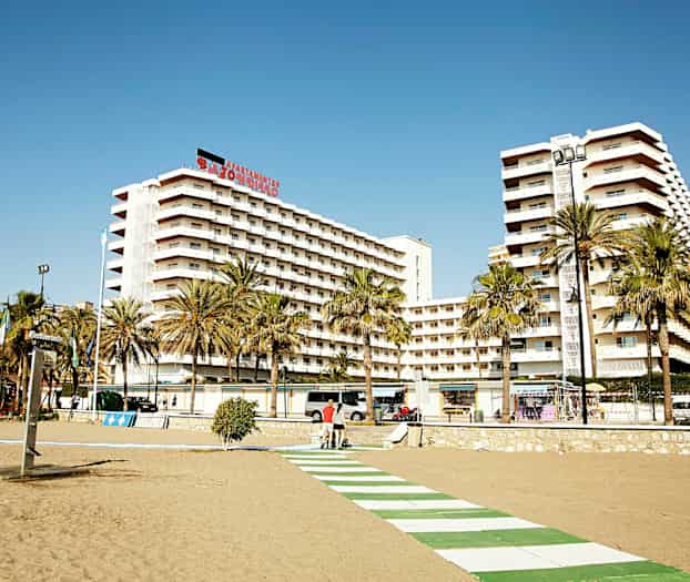 Kävelytie rannalla korkeiden asuinrakennusten edessä, etualalla palmuja. (Tekoälyn luoma teksti)