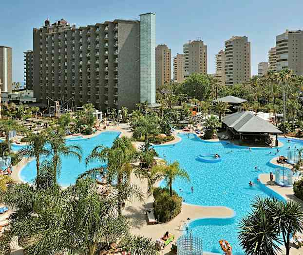 Hotellialue, jossa suuri uima-allas ja aurinkotuoleja, ympärillä palmuja ja korkeita rakennuksia. (Tekoälyn luoma teksti)