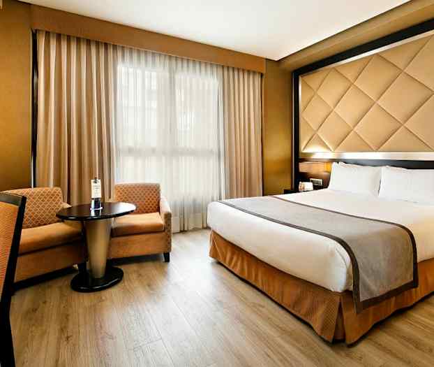 Hotellihuone, jossa on parivuode, pöytä kahdella tuolilla ja ikkuna verhoilla. (Tekoälyn luoma teksti)