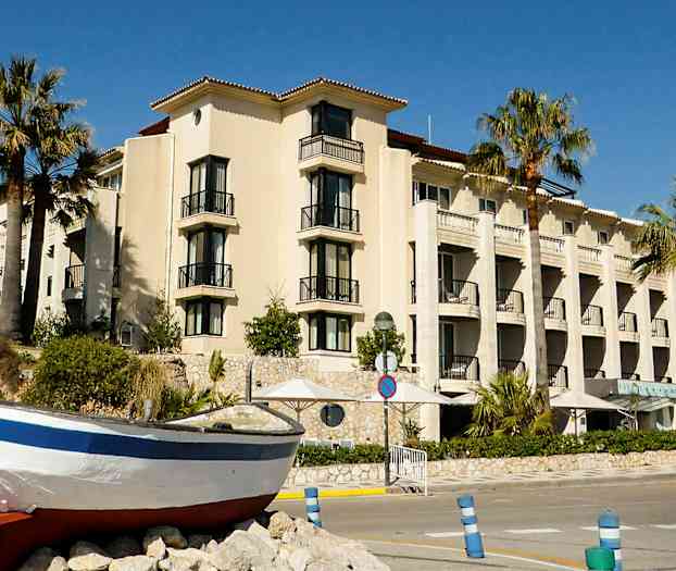 Rakennus, jossa on parvekkeita ja palmuja sen edessä, sekä vene maalla. (Tekoälyn luoma teksti)