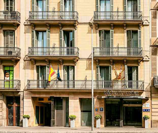 Rakennuksen etuosa parvekkeineen, sisäänkäynti vasemmalla ja hotellin kyltti sisäänkäynnin luona. (Tekoälyn luoma teksti)