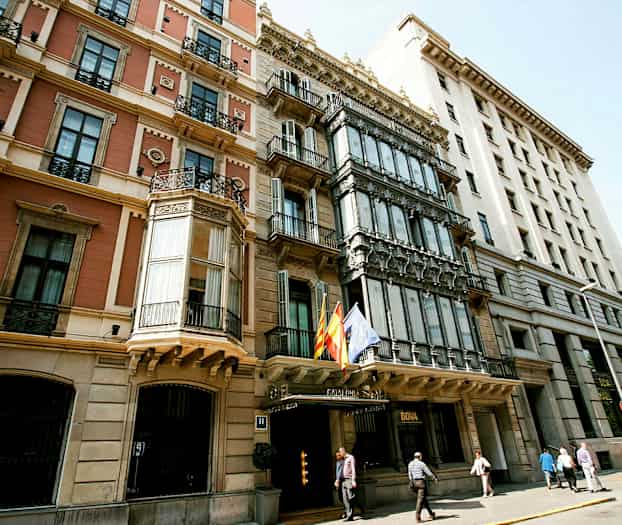 Kuva useiden historiallisten rakennusten julkisivusta, joissa on erilaisia arkkitehtonisia tyylejä, ja ulkona liehuvat liput. (Tekoälyn luoma teksti)