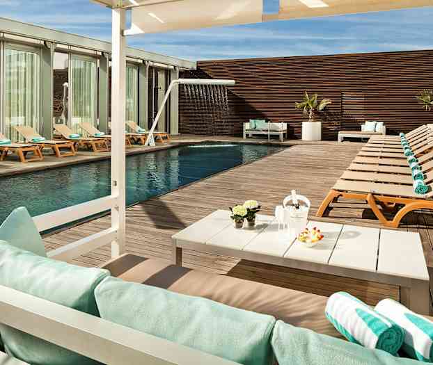 Ulkouima-allas, jonka ympärillä on aurinkotuoleja ja pyyhkeitä puukannella sekä pöytä koristeilla ja aurinkovarjo. (Tekoälyn luoma teksti)