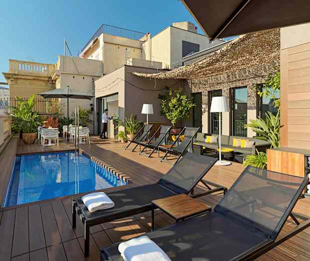 Kattoterassi, jossa aurinkotuoleja, pieni suorakaiteen muotoinen uima-allasalue, kasveja ja pöytiä varjoineen. (Tekoälyn luoma teksti)