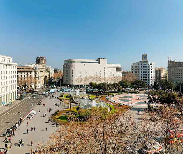 Kuva aukiosta, jota ympäröivät rakennukset; aukion keskellä on suihkulähde, ja ihmiset kävelevät ympäriinsä. (Tekoälyn luoma teksti)