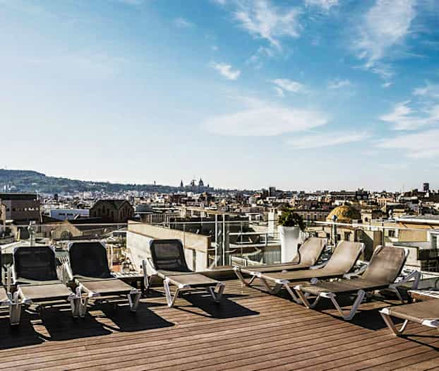 Aurinkotuoleja kattoterassilla, näkymä kaupunkimaisemaan. (Tekoälyn luoma teksti)