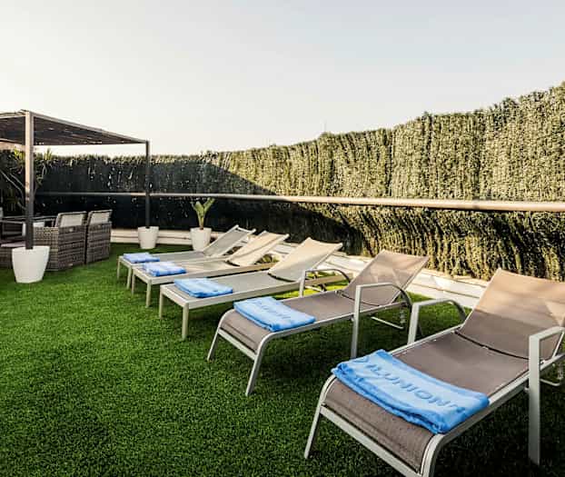 Aurinkotuoleja ja nojatuoleja puutarhaympäristössä, jossa on tekonurmi. (Tekoälyn luoma teksti)