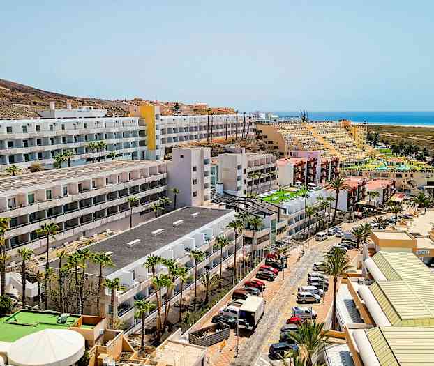 Hotellirakennuksia lähellä merta, pysäköityjä autoja ja palmuja. (Tekoälyn luoma teksti)