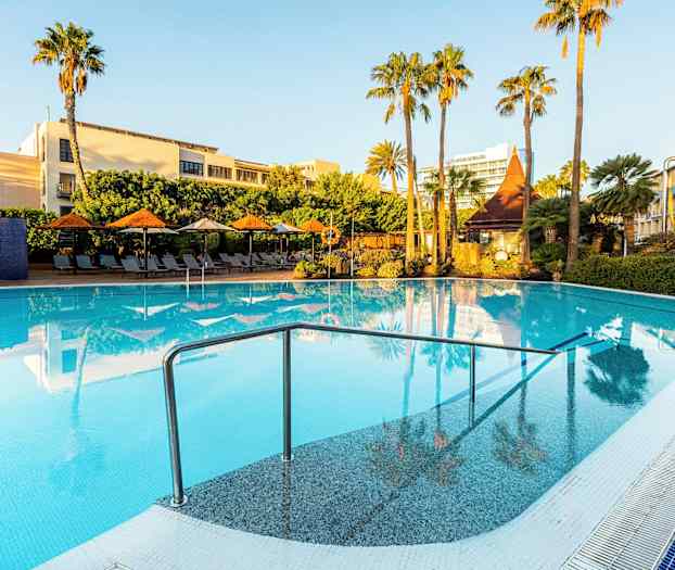 Ulkouima-allas, jota ympäröivät aurinkotuolit, aurinkovarjot ja vihreät palmut kirkkaan sinisen taivaan alla. (Tekoälyn luoma teksti)