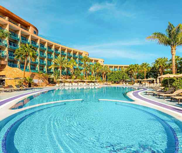 Hotellin uima-allasalue aurinkotuoleineen ja palmupuineen rakennuksen parvekkeiden edustalla. (Tekoälyn luoma teksti)