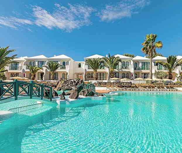 Vaaleansininen uima-allas valkoisten rakennusten edessä, palmuja ja kirkas taivas taustalla. (Tekoälyn luoma teksti)