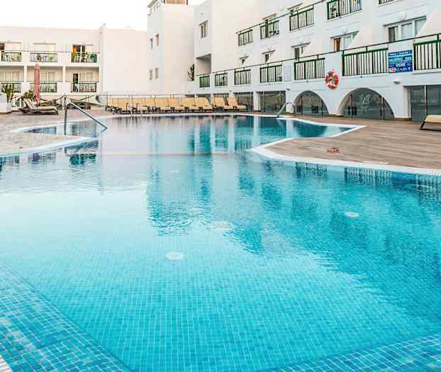 Ulkouima-allas lomakeskuksessa, jossa on aurinkotuoleja ja taustalla valkoisia rakennuksia. (Tekoälyn luoma teksti)