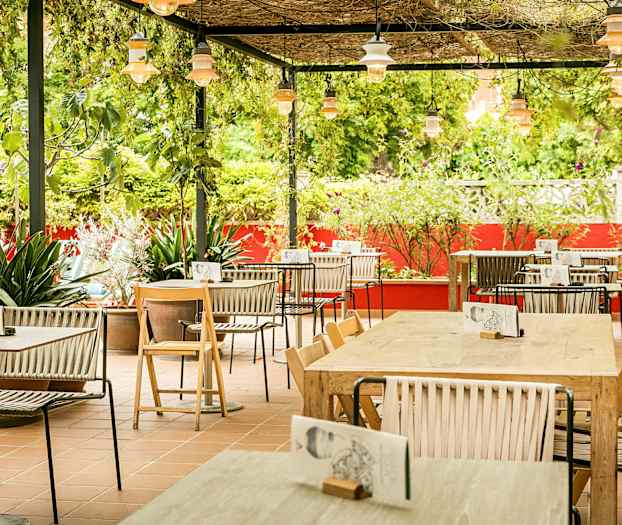 Ulkoterassi, jossa on pöytiä ja tuoleja, vihreyden ja punaisten seinien ympäröimänä. (Tekoälyn luoma teksti)