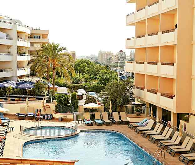 Hotelli, jossa ulkouima-allas ja aurinkotuoleja, ympärillä vihreitä puita ja kerrostaloja. (Tekoälyn luoma teksti)