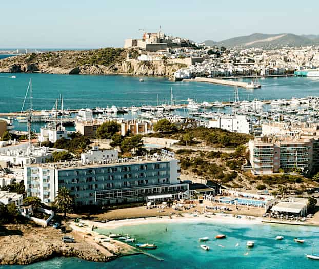 Rannikolla sijaitseva kaupunki, jossa on useita rakennuksia ja venesatama; edustalla näkyy pieniä veneitä ja ranta. (Tekoälyn luoma teksti)