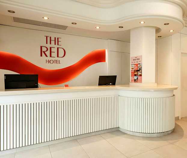Hotellin vastaanotto valkoisilla kalusteilla ja punainen logo seinällä. (Tekoälyn luoma teksti)