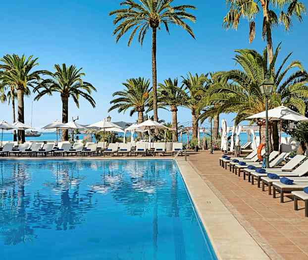 Ulkouima-allas, jota ympäröivät aurinkotuolit, aurinkovarjot ja palmut, taustalla meri. (Tekoälyn luoma teksti)