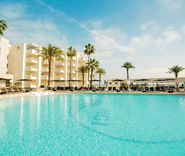 Suuri uima-allas modernin hotellin edessä, ympärillä palmuja sinisen taivaan alla. (Tekoälyn luoma teksti)