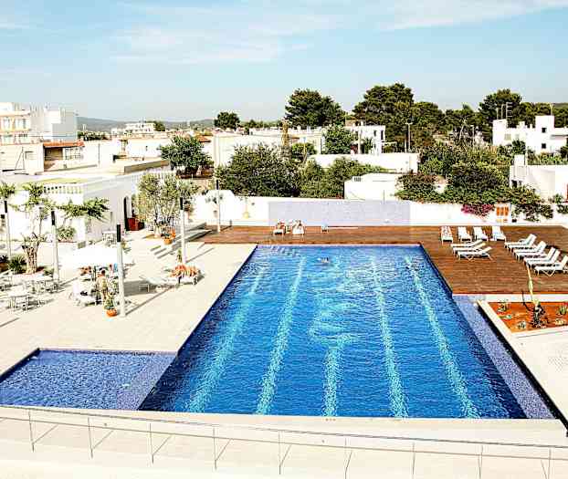 Ulkouima-allas, jossa on siniset laatat, aurinkotuoleja ja valkoisia rakennuksia ympärillä. (Tekoälyn luoma teksti)