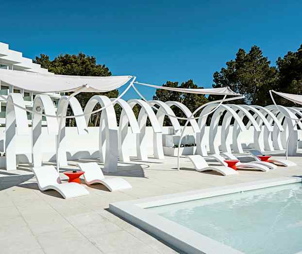 Valkoinen arkkitehtuuri kaarineen, aurinkotuoleja ja punaisia pöytiä altaan äärellä. (Tekoälyn luoma teksti)