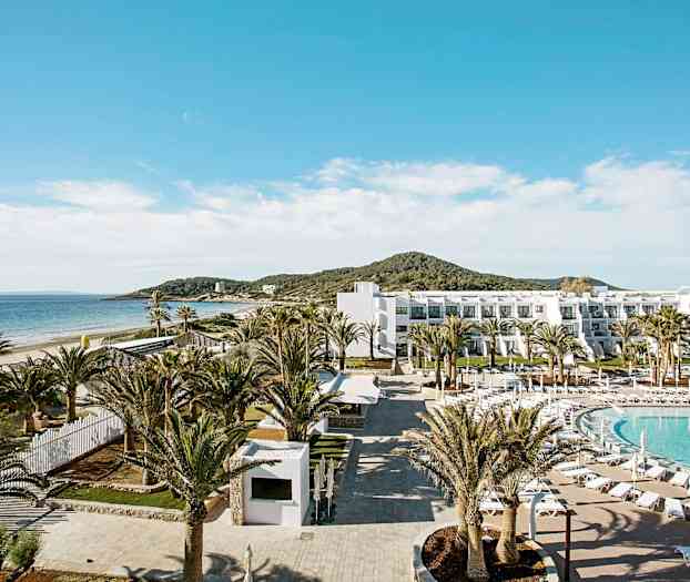 Hotellialue rannalla, jossa on uima-allas, palmuja ja valkoinen rakennus. (Tekoälyn luoma teksti)