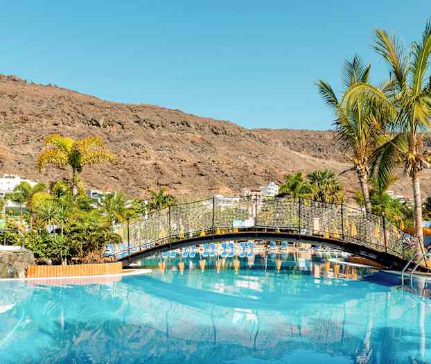 Uima-allas, jossa on silta ja palmuja ympäröitynä vuorilla. (Tekoälyn luoma teksti)