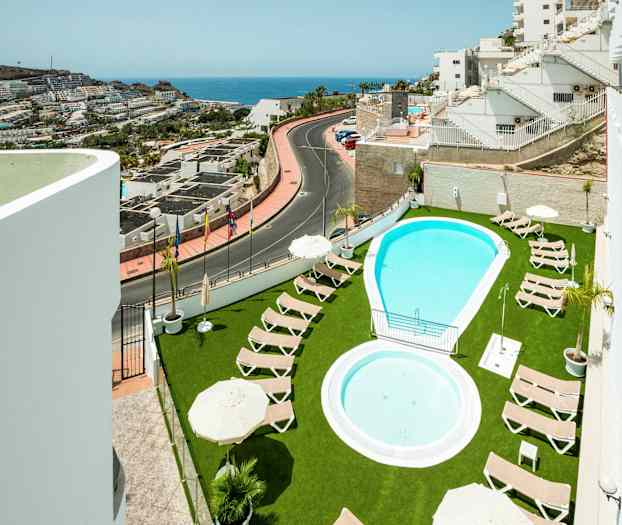 Ulkouima-allas, jonka ympärillä aurinkotuoleja vihreällä nurmella, näkymät lähirakennuksiin ja merelle. (Tekoälyn luoma teksti)