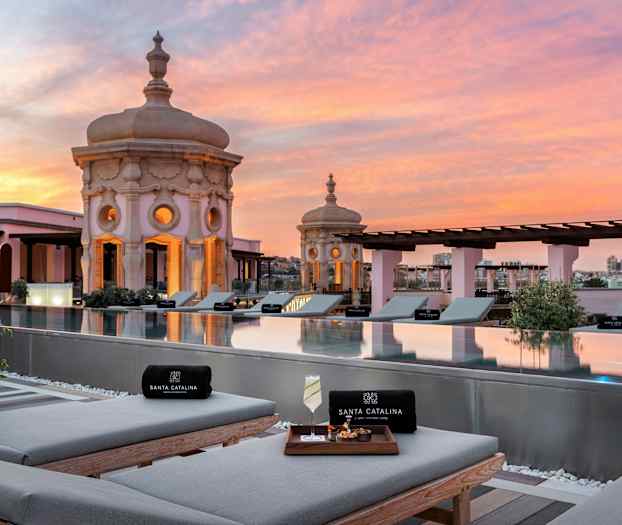 Näköala kattoterassin altaalle, jossa aurinkotuoleja ja koristeellisia kupoleja auringonlaskussa. (Tekoälyn luoma teksti)