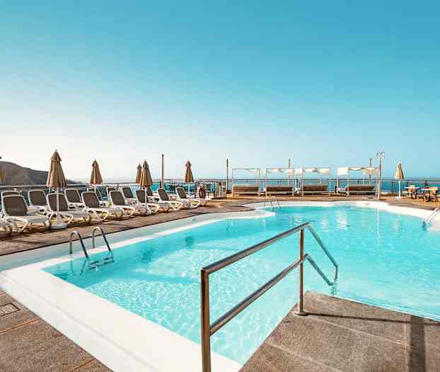 Uima-allasalue, jossa aurinkotuoleja ja aurinkovarjoja sekä näkymä merelle. (Tekoälyn luoma teksti)