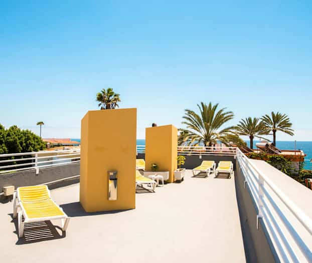 Kattoterassi aurinkotuoleineen, josta on näkymä palmuihin ja mereen. (Tekoälyn luoma teksti)