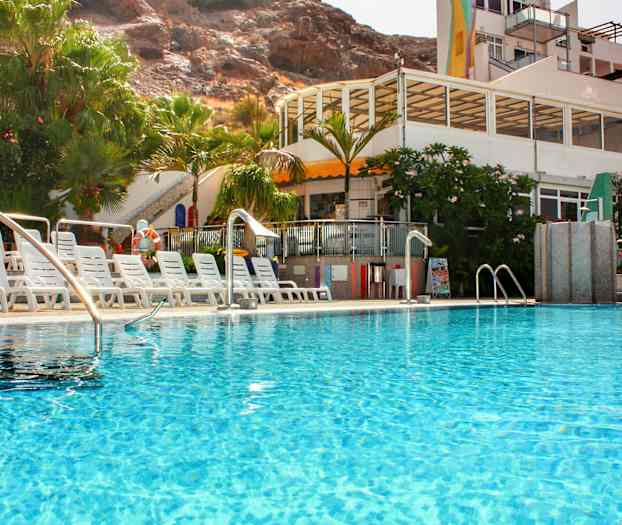 Ulkouima-allas, jota ympäröivät aurinkotuolit ja vehreys, taustalla rakennus. (Tekoälyn luoma teksti)