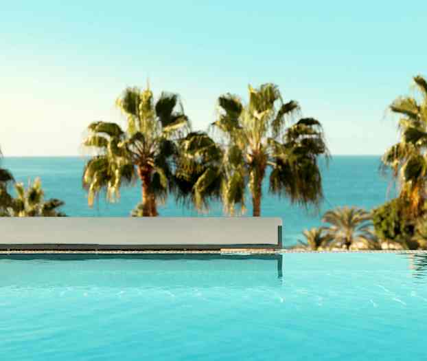 Uima-allas kirkkaalla vedellä etualalla ja palmuja sekä meri taustalla. (Tekoälyn luoma teksti)