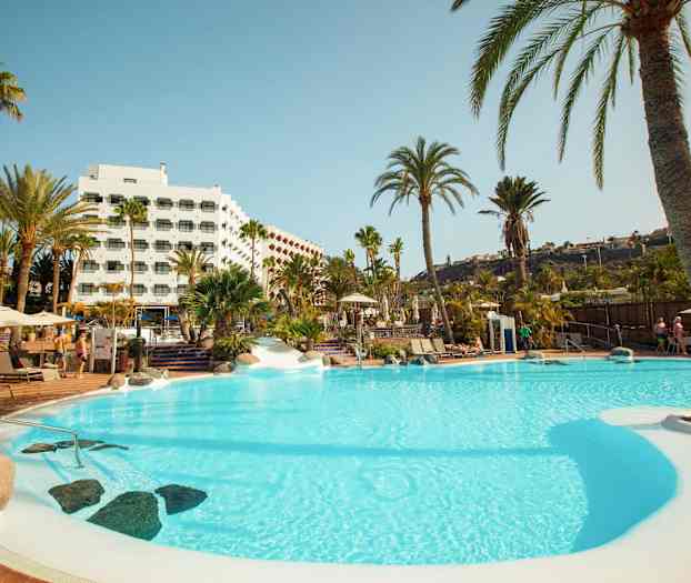 Uima-allas, jota ympäröivät palmupuut ja hotelli taustalla. (Tekoälyn luoma teksti)