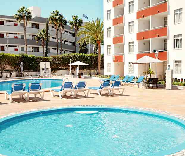 Ulkouima-allas, jota ympäröivät aurinkotuolit, rakennus taustalla. (Tekoälyn luoma teksti)