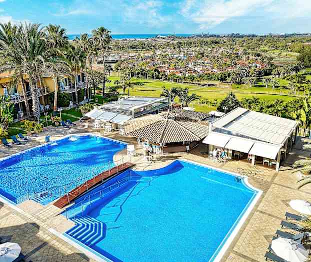 Kuva hotellin uima-altaasta, jossa on aurinkotuoleja, varjoja ja ympäröiviä rakennuksia. (Tekoälyn luoma teksti)