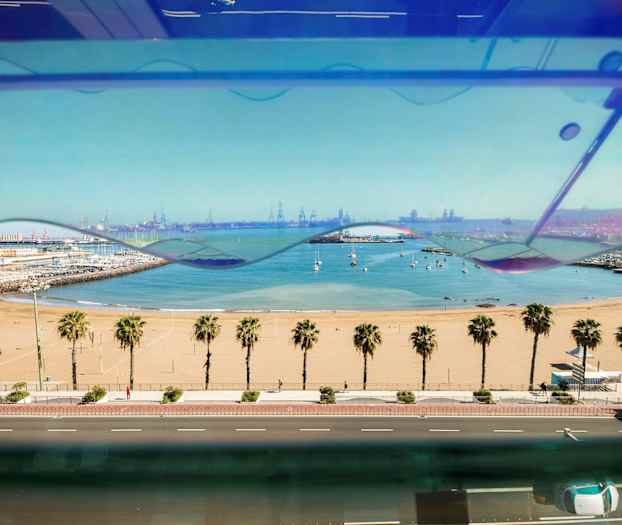 Näköala hiekkarannalle, jossa palmuja, etualalla tie ja taustalla satama sekä venesatama. (Tekoälyn luoma teksti)